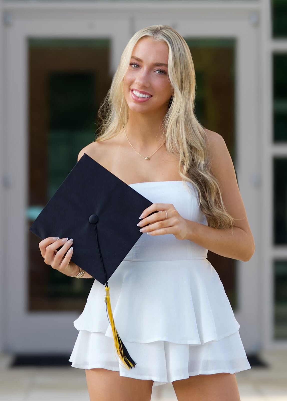 Graduate holding a cap in front of her school