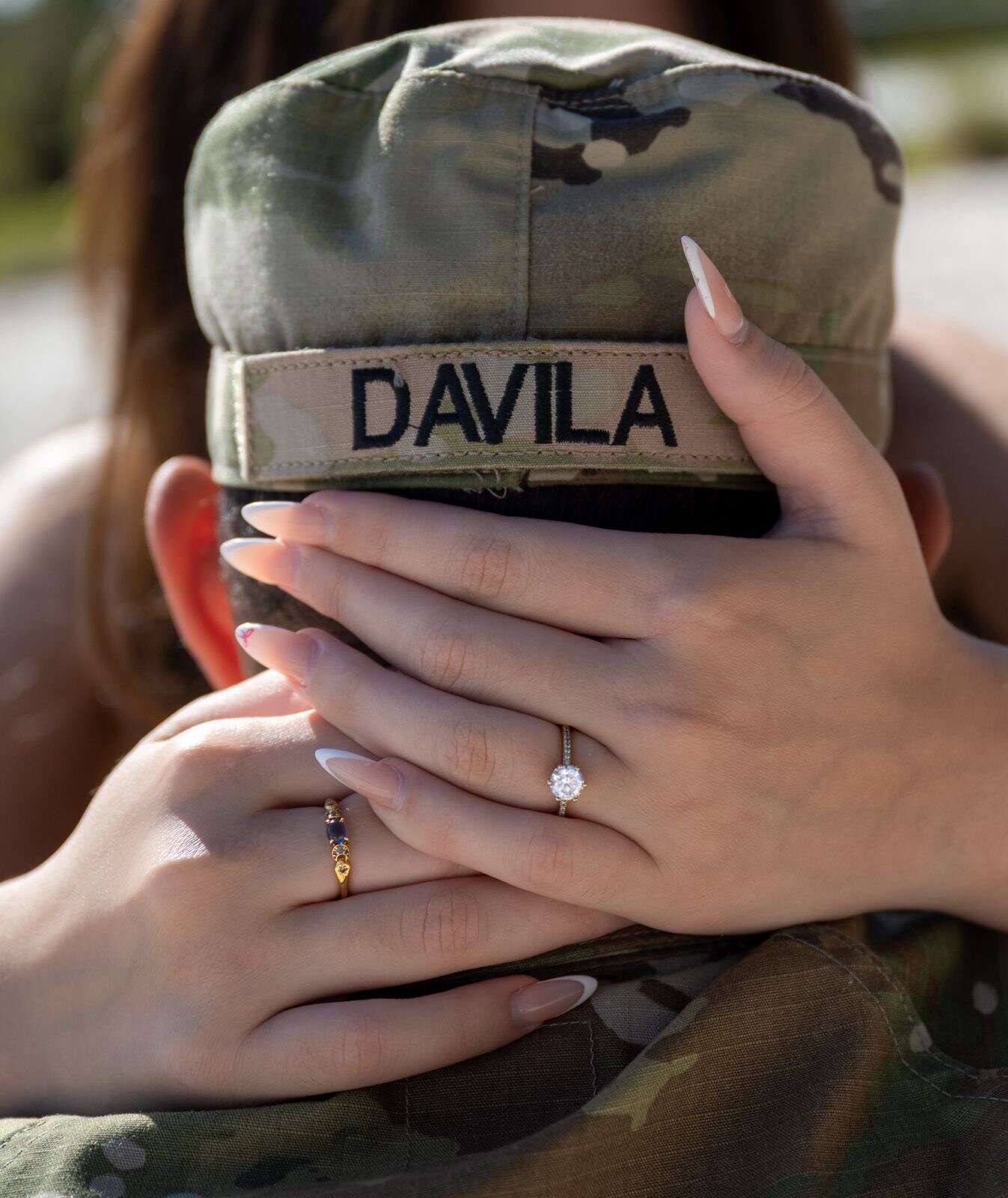 Engagement ring and hands resting over a military name tape
