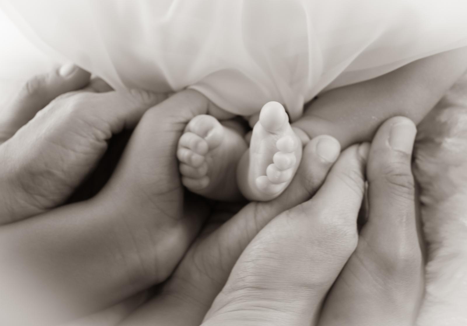 Pés de um bebê recém-nascido acolhidos pelas mãos de sua família em um retrato em preto e branco