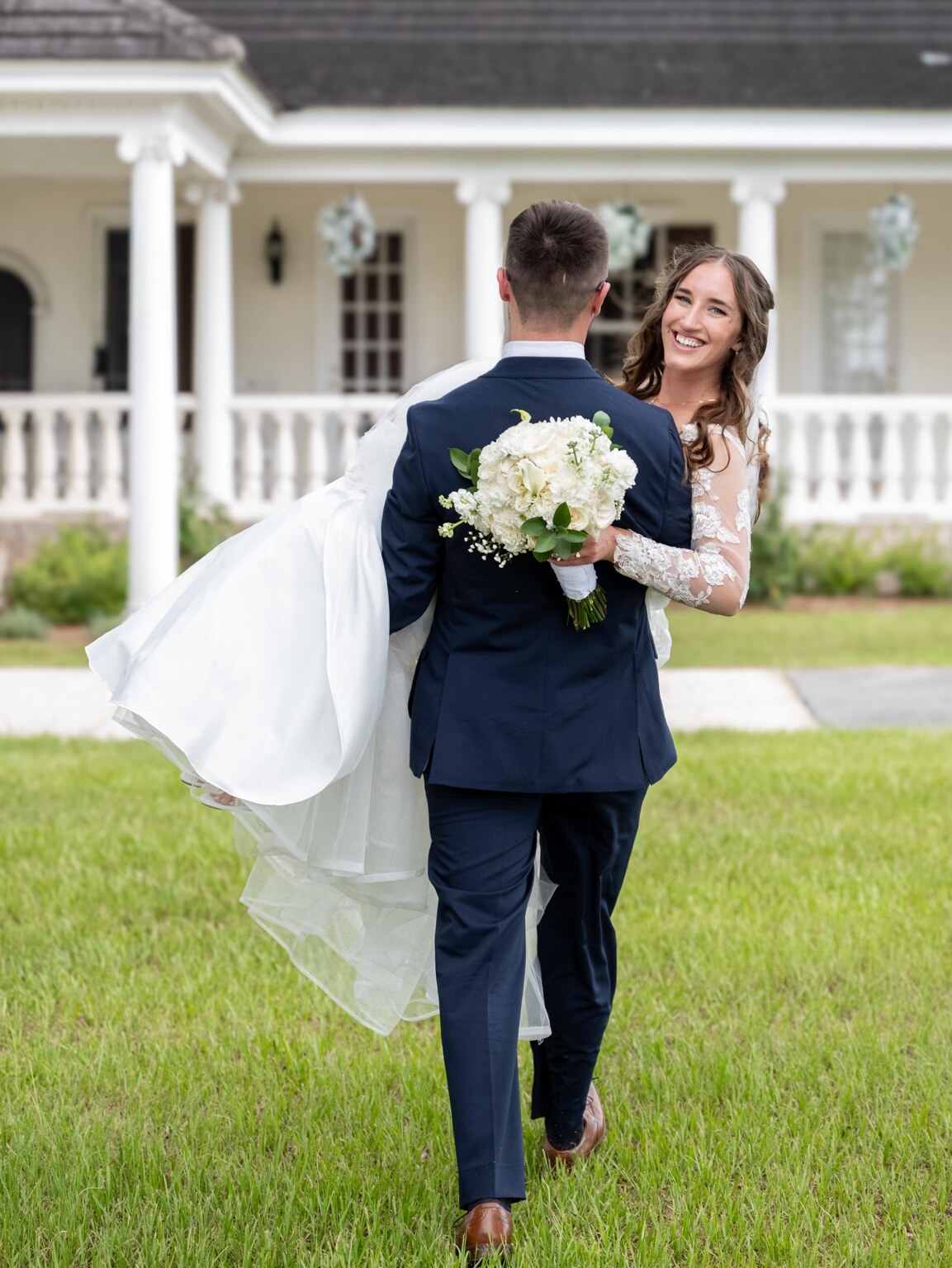 Groom carrying his smiling bride across a lawn