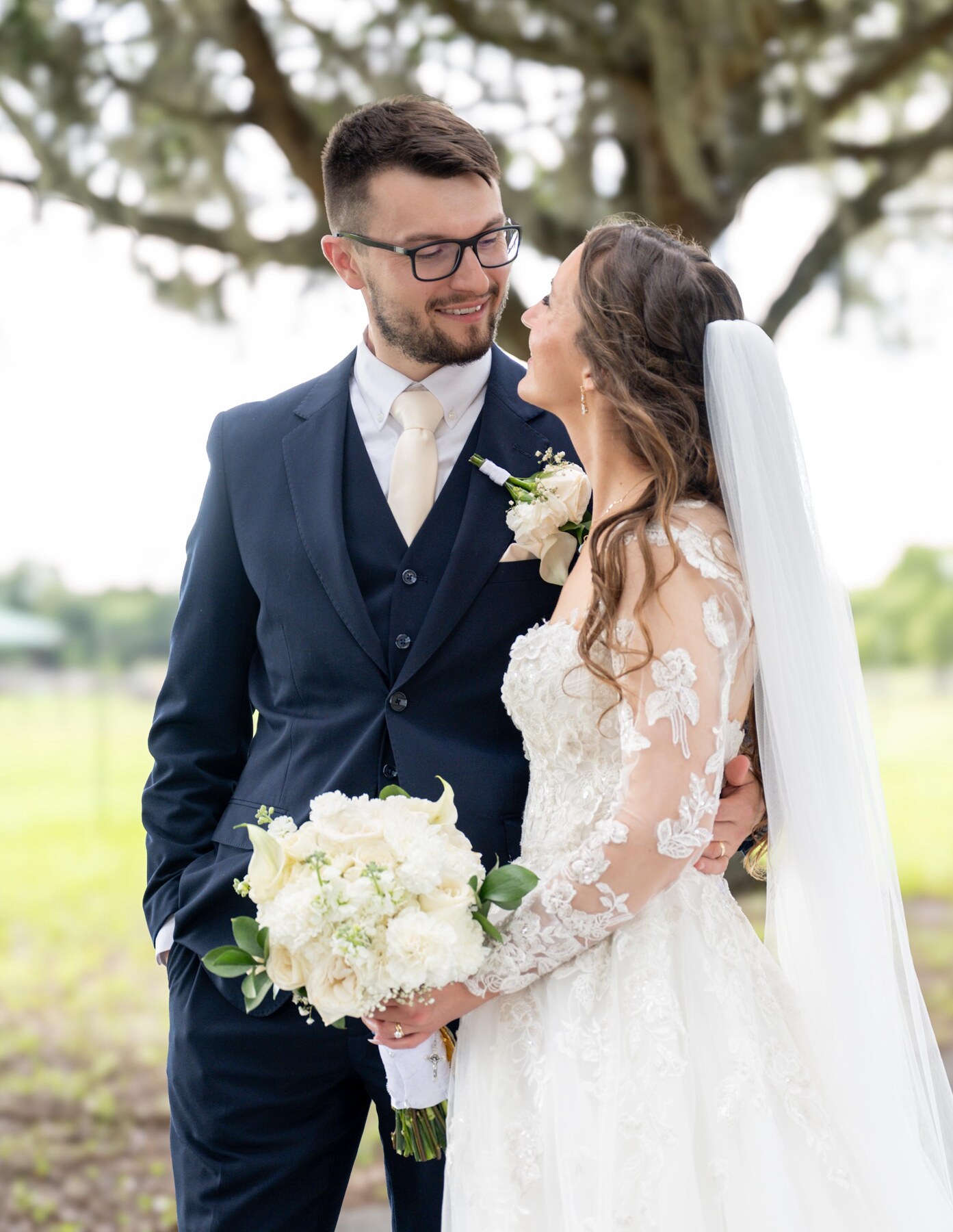 Newlyweds sharing a joyful look beneath a sprawling oak tree